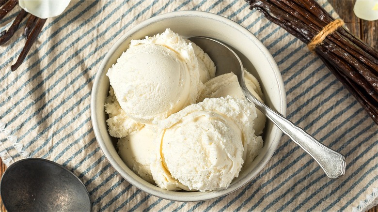 Scoops of vanilla ice cream in a white bowl with a metal spoon