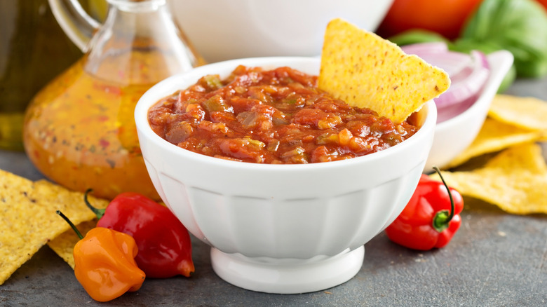 Tortilla chip dipped into spicy tomato salsa in a white bowl