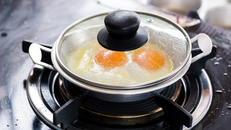 Frying eggs in pan with lid