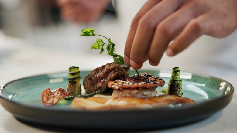 A hand adding garnish to a plate.