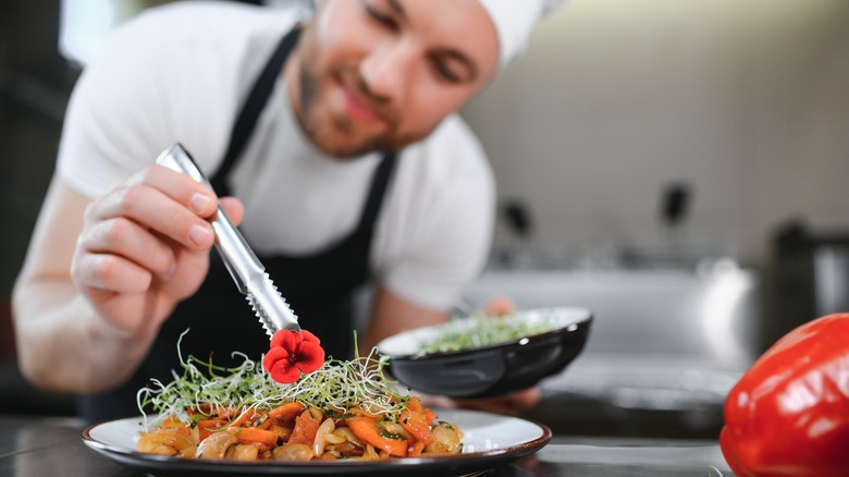 A chef garnishing a plate in a kitchen.