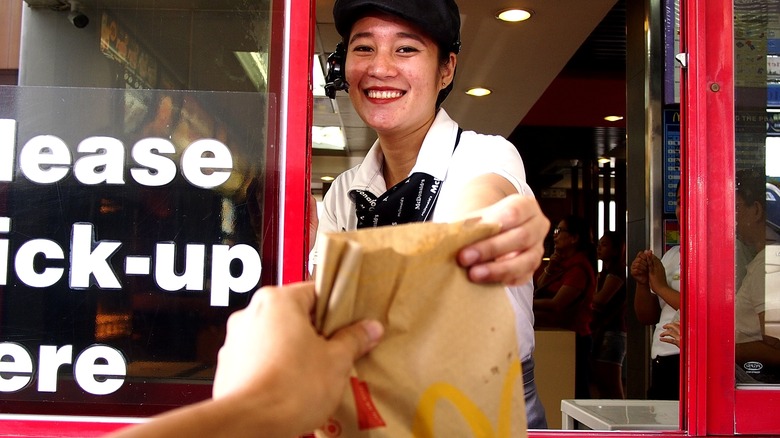Smiling drive-thru employee handing food to customer