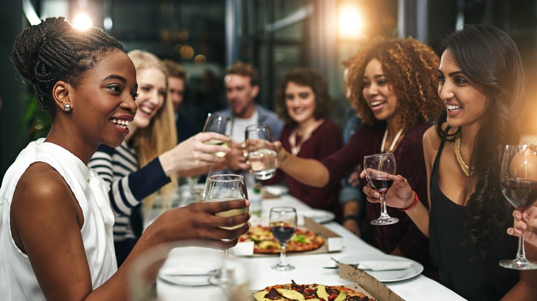 A large group of people sit at a fine dining restaurant, clinking wine glasses and talking