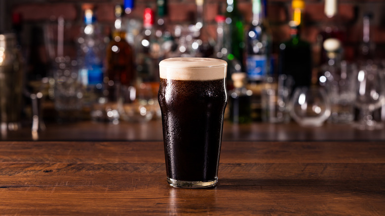 Dark beer with foamy head in a tall glass sits on a bartop.