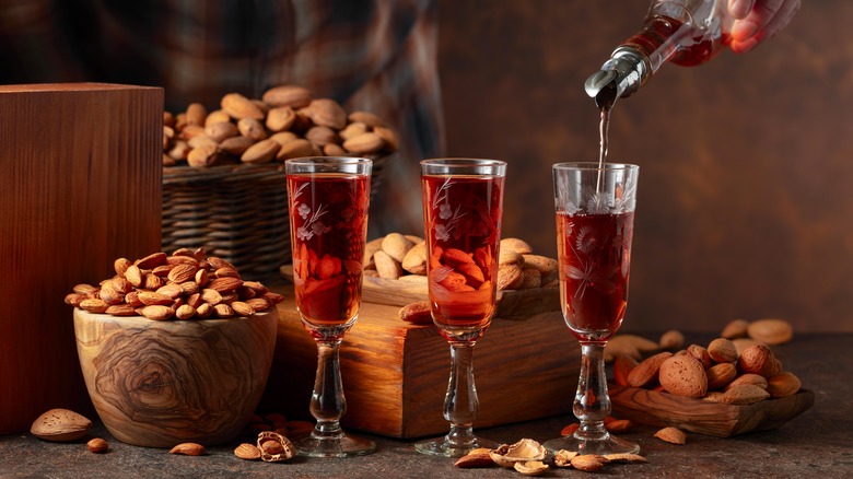 Amaretto being poured into three long-stemmed shot glasses with almonds in the background