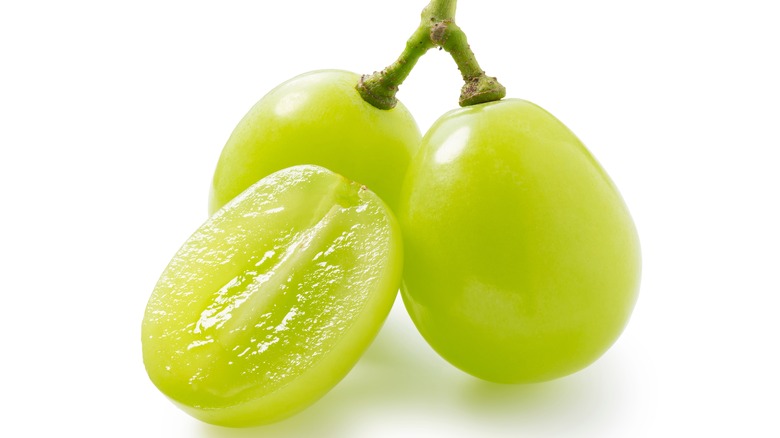 Two green grapes on stem next to cut grape