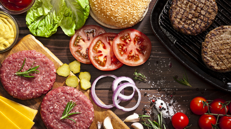 Raw and cooked beef patties with ingredients for making burgers