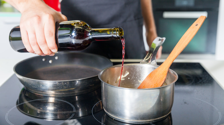 Pouring red wine into pan to make sauce