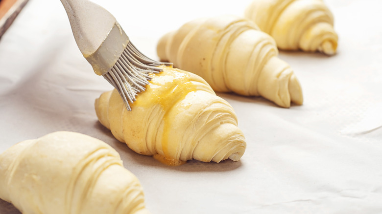 Egg wash being brushed onto croissants