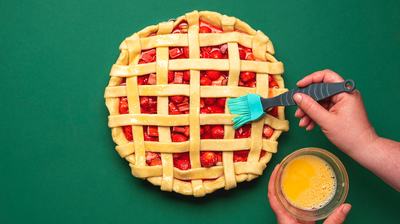 Egg wash being brushed onto a lattice strawberry rhubarb pie crust