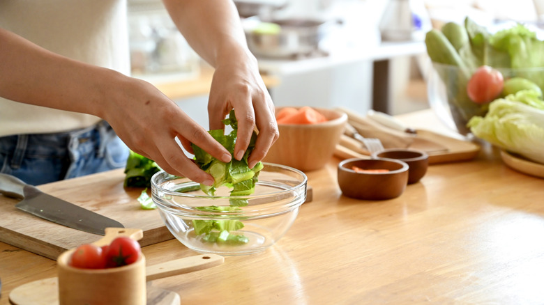 A chef adding lettuce to a bowl to make a salad