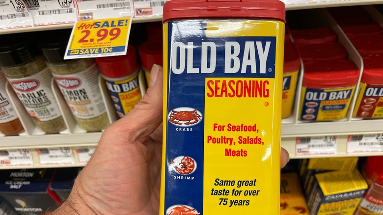 A hand holding a tin container of Old Bay Seasoning near a grocery store shelf