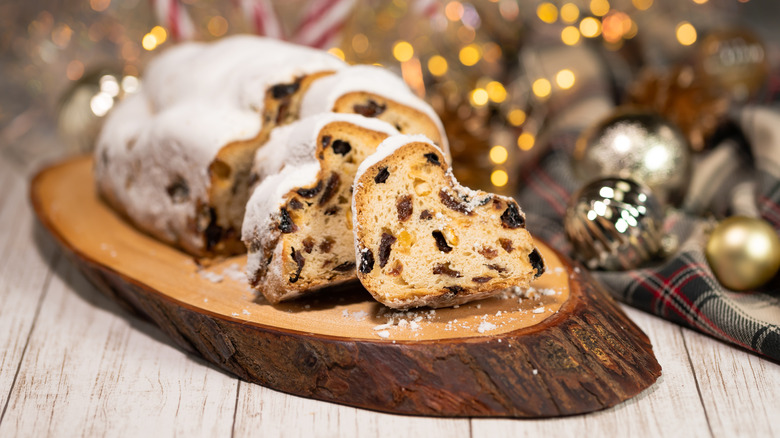 Christmas stollen cut into slices on a board with Christmas decorations in the background