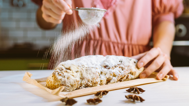 Person's hands sprinkling powdered sugar onto a baked Christmas stollen