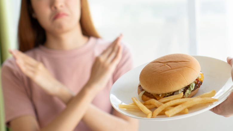 A woman refusing a fast food burger and fries