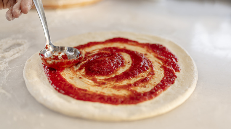 adding pizza sauce to dough