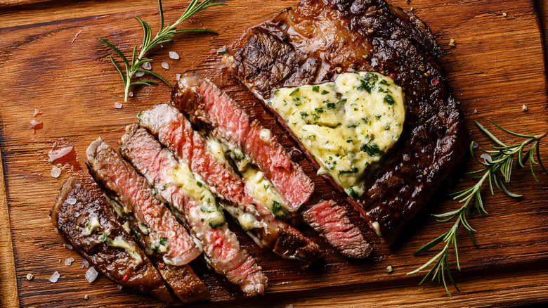 sliced steak with herb butter on cutting board