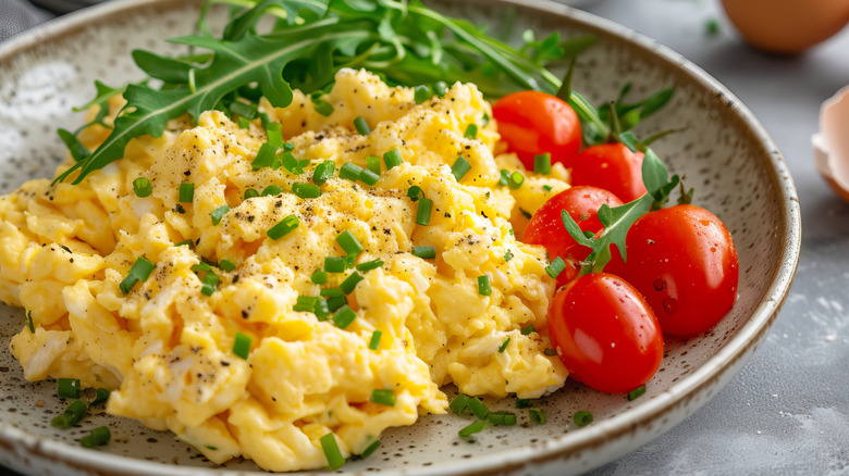 Scrambled eggs on a plate with chives and cherry tomatoes