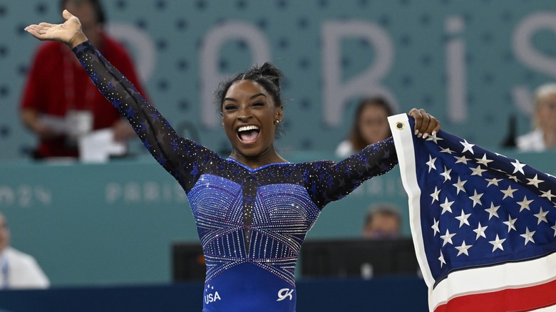 Simone Biles smiles while holding American flag