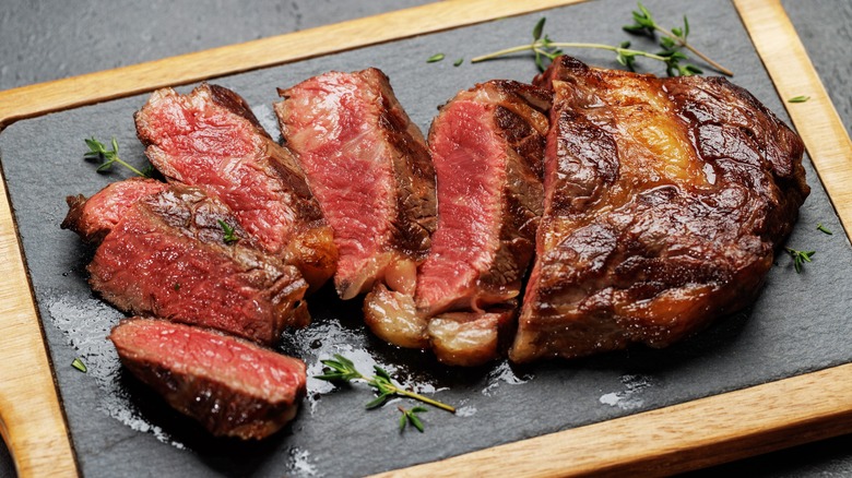Sliced ribeye steak on platter with fresh thyme