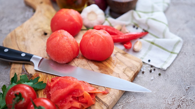 Peeled tomatoes on a cutting board with knife