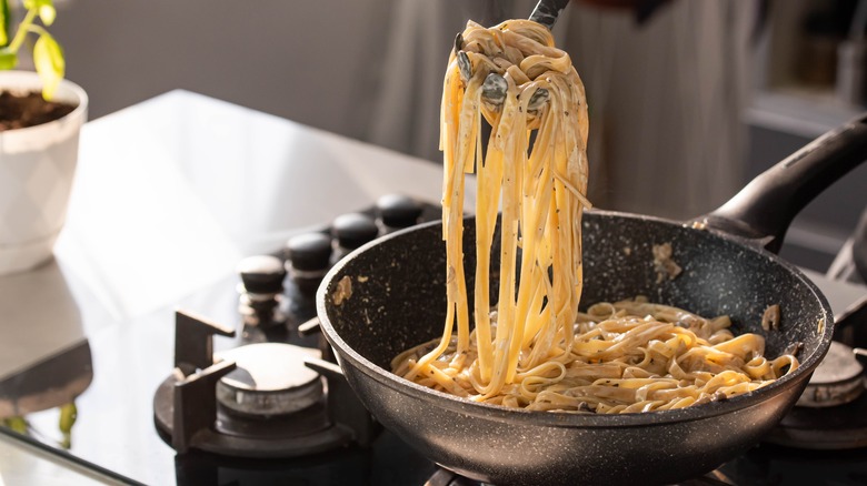 Tagliatelle and sauce being tossed together on stove