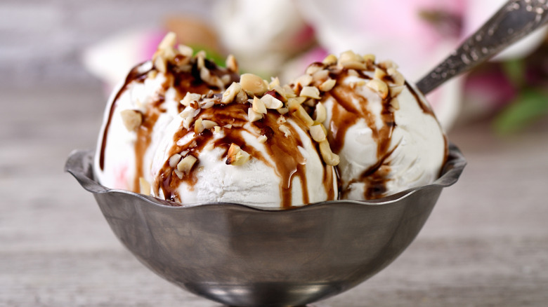 a silver bowl of plombir ice cream topped with nuts and chocolate syrup