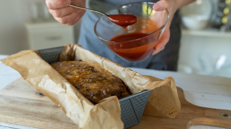 a person with a bowl of glaze about to top a meatloaf