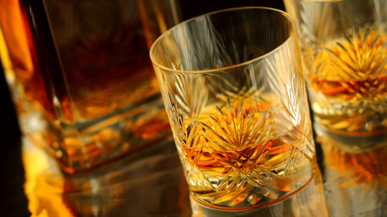 A glass of whiskey served neat with another glass and bottle of whiskey in background