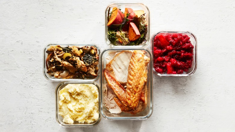 Roast vegetables, turkey, stuffing, mashed potatoes, and cranberry sauce in glass containers