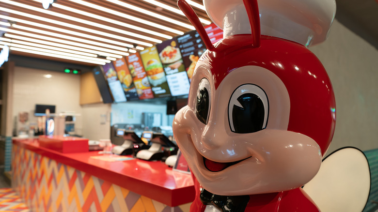 A jollibee mascot statue stands in front of a Jollibee fast food counter