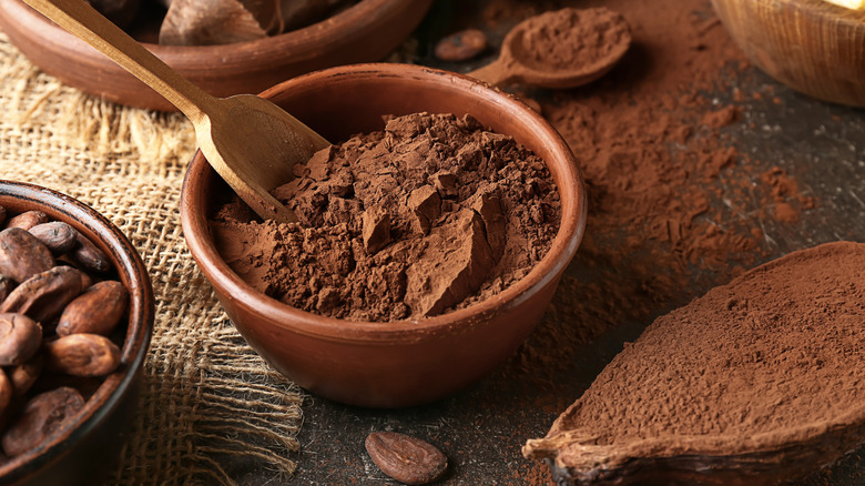 Chocolate cocoa powder in wooden bowl with spoon on table with whole beans