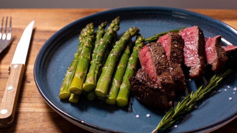 Medium rare steak with seasonal asparagus on a black plate