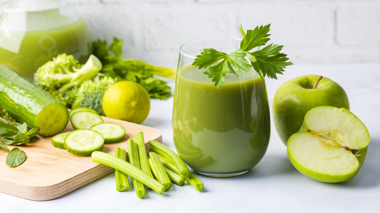 Glass of green juice with sprig of parsley, apple, celery, cucumber