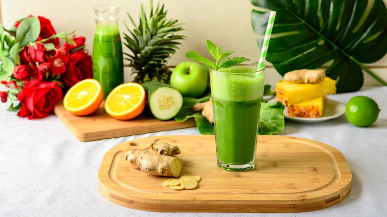 Green juice in glass with straw with fruits and vegetables in background