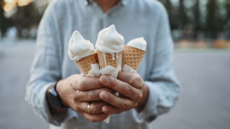 three vanilla ice cream cones melting in hands 