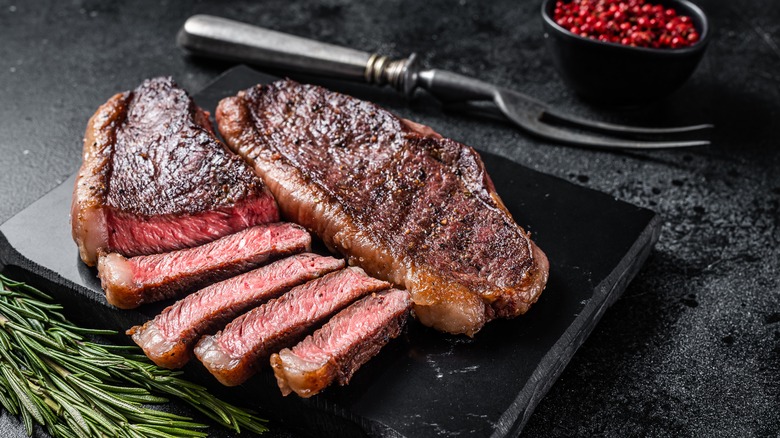 Partially sliced rare steak on black platter