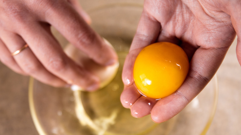 Hands holding separated egg yolk with egg whites in bowl
