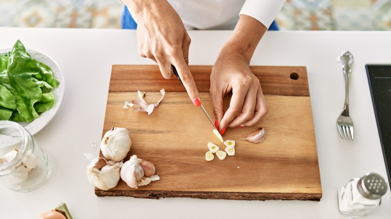 hands slicing garlic on cutting board