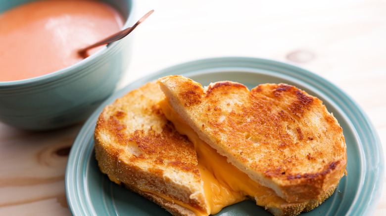 grilled cheese on a plate with a bowl of tomato soup
