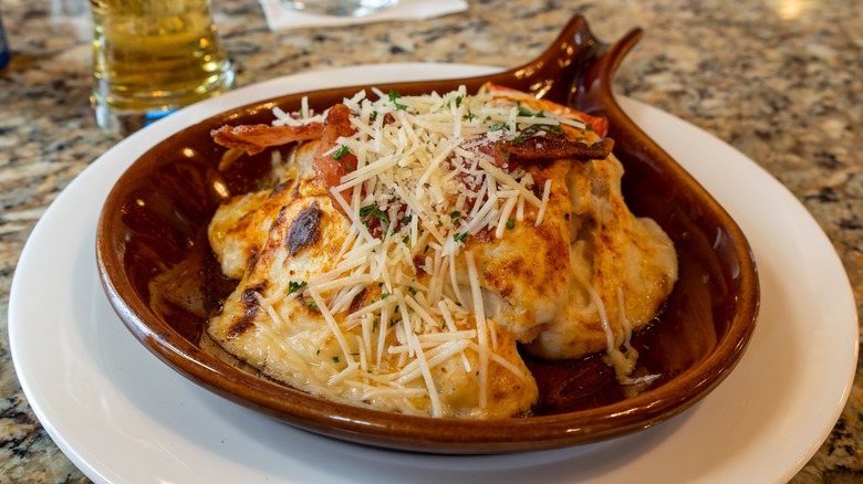 A Hot Brown served in a brown ceramic dish with a handle that is placed on a white plate