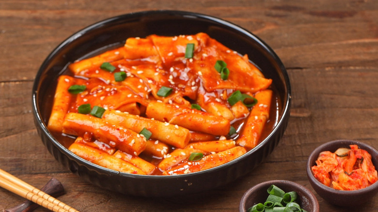 A bowl of tteokbokki with sides of kimchi and green onions