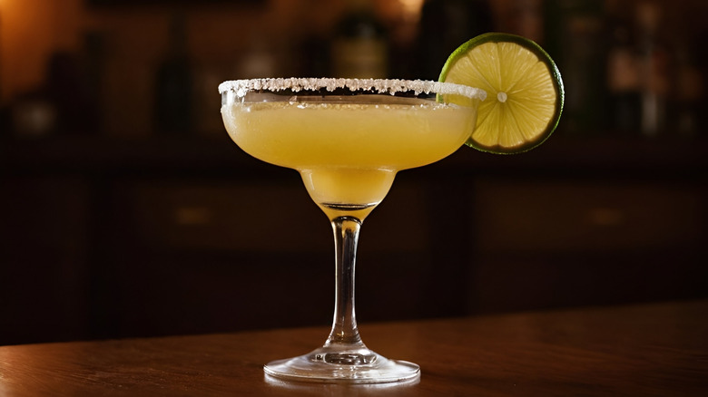 Margarita served in a glass with a salted rim and a lime wheel hanging on the side, with a blurred restaurant-style background