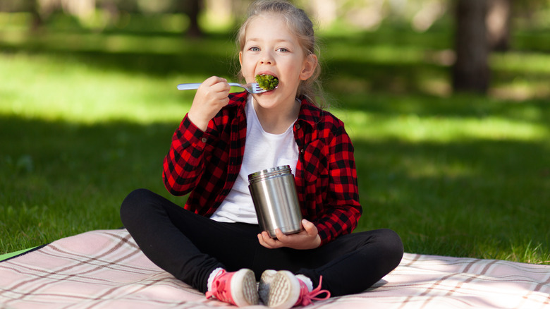 Child eating broccoli from thermos