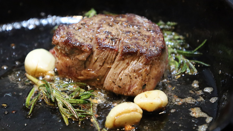 Small piece of seared steak in a cast iron pan with garlic and rosemary