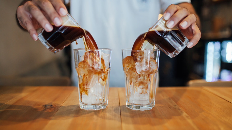 Person adding two espresso shots to two glasses filled with ice