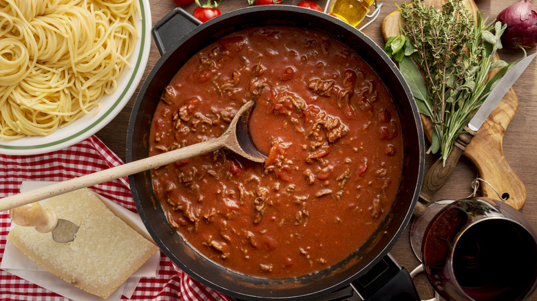 Pot of Bolognese sauce surrounded by pasta, cheese, and herbs