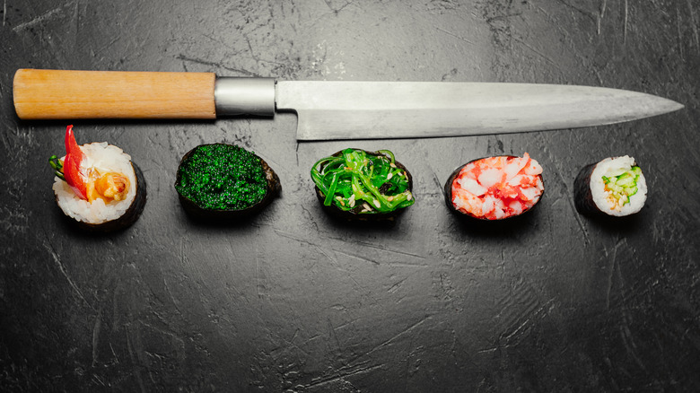 A yanagiba knife next to an assortment of sushi on black surface