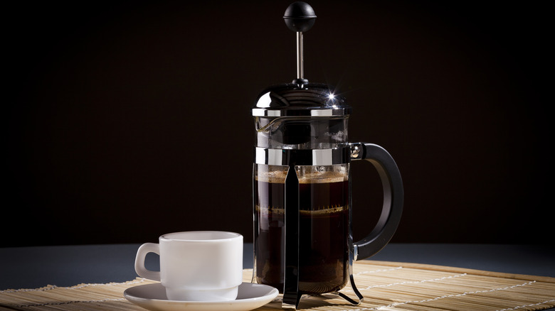 A French press next to a white cup