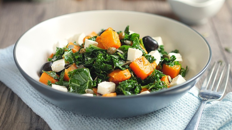 Warm kale salad in a shallow bowl with cooked squash, olives, and cubes of feta cheese